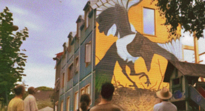 People looking at a 3 three-story-high mural of a magpie.